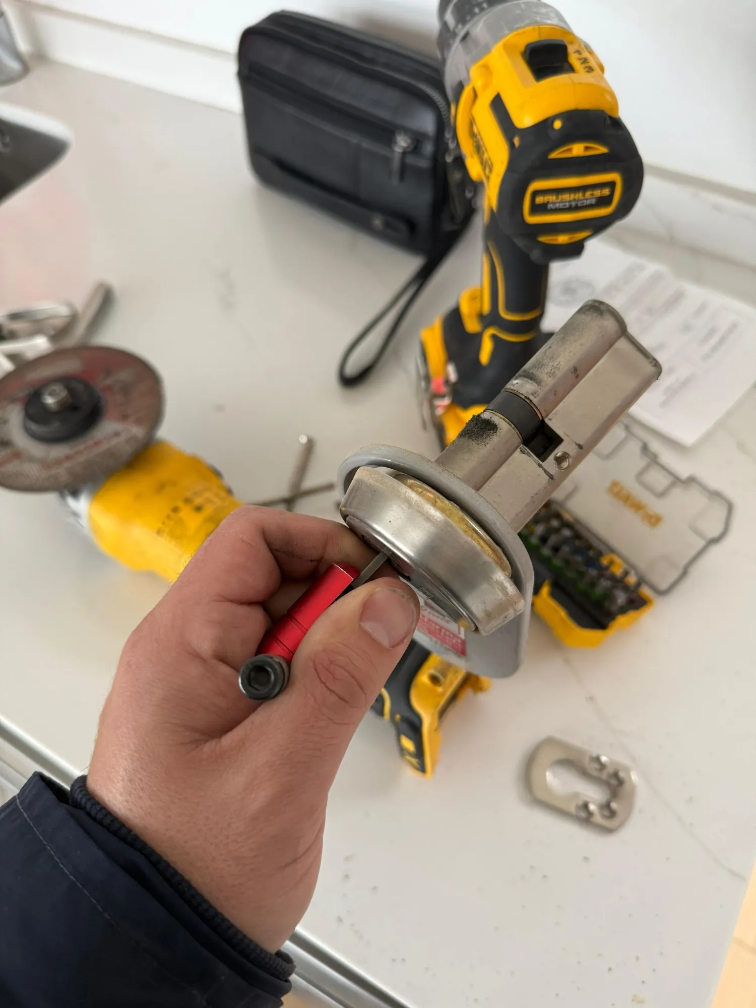 Bombín de seguridad desmontado con su escudo protector en la mano de uno de nuestros técnicos en Rivas-Vaciamadrid, con el taladro y la radial sobre la encimera.