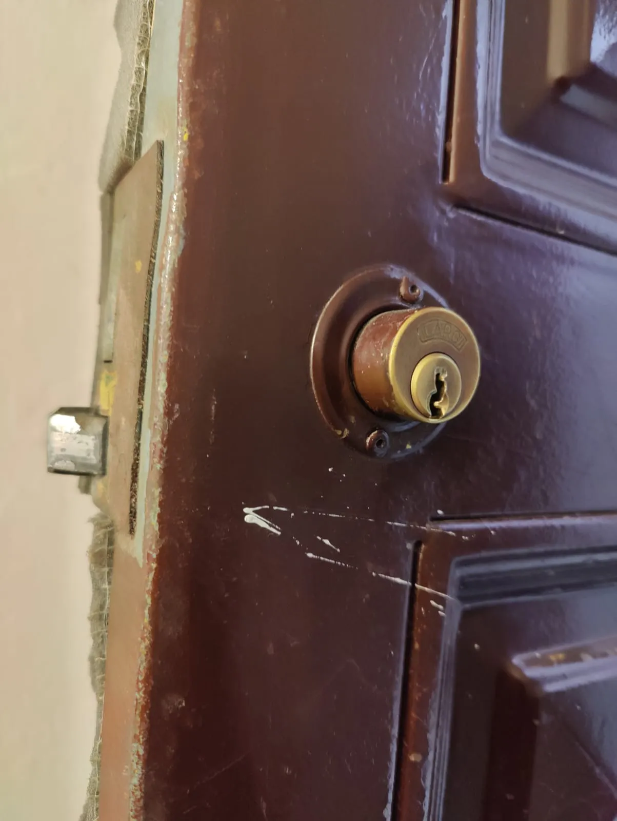 Bombín redondo de latón en una puerta marrón en Collado Villalba, con arañazos en la pintura y el pestillo asomando por el canto.