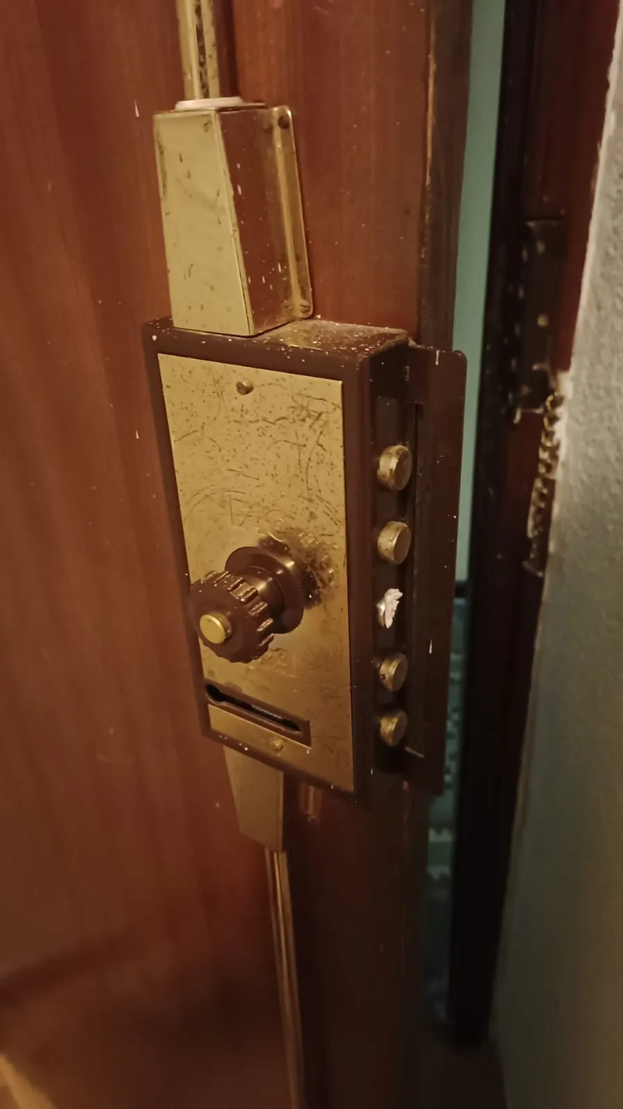 Cerradura de seguridad de sobreponer, con pomo, cinco bulones laterales y barras verticales hacia el suelo y el techo, en una puerta de madera en Alcalá de Henares.