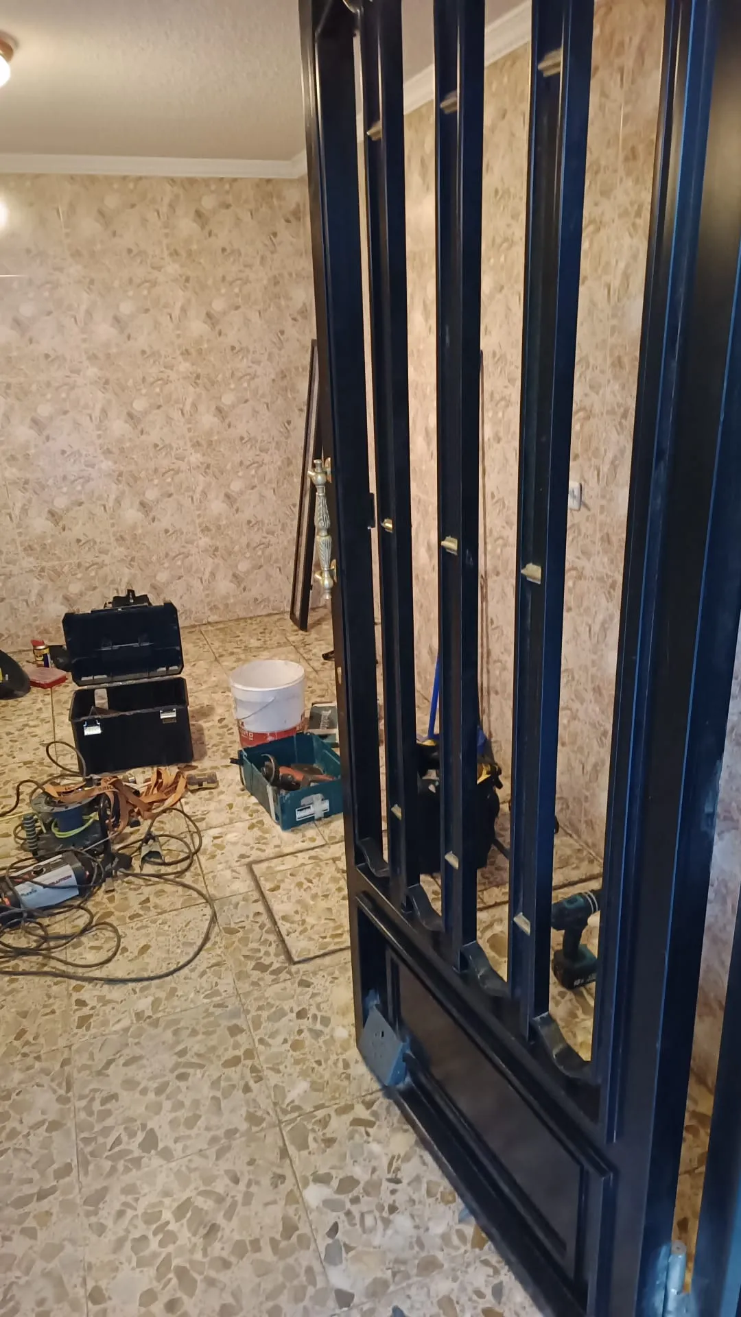 Puerta de reja metálica negra abierta durante un trabajo de cerrajería en Alcorcón, con cajas de herramientas, herramientas eléctricas y cables en el suelo.